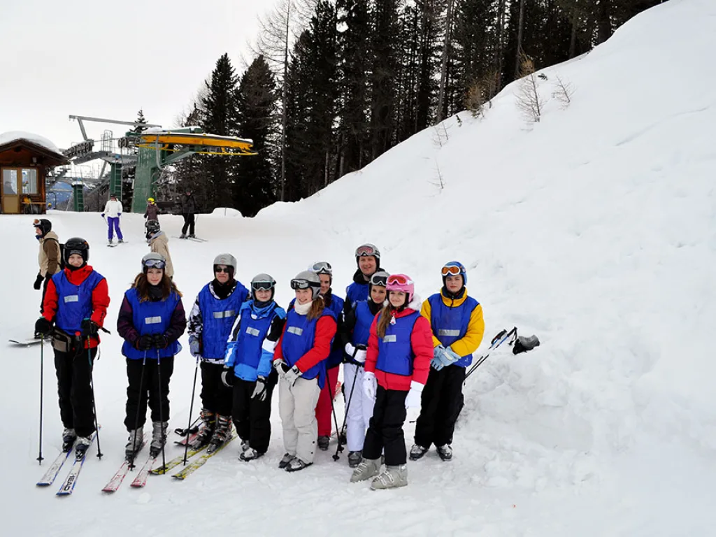 Kleinere Skigruppe steht am Pistenrand vor dem Wald.